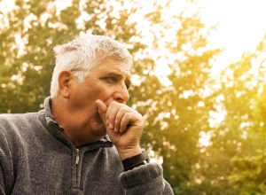 Coughing Senior Man on fresh air, considering symptoms of coronavirus