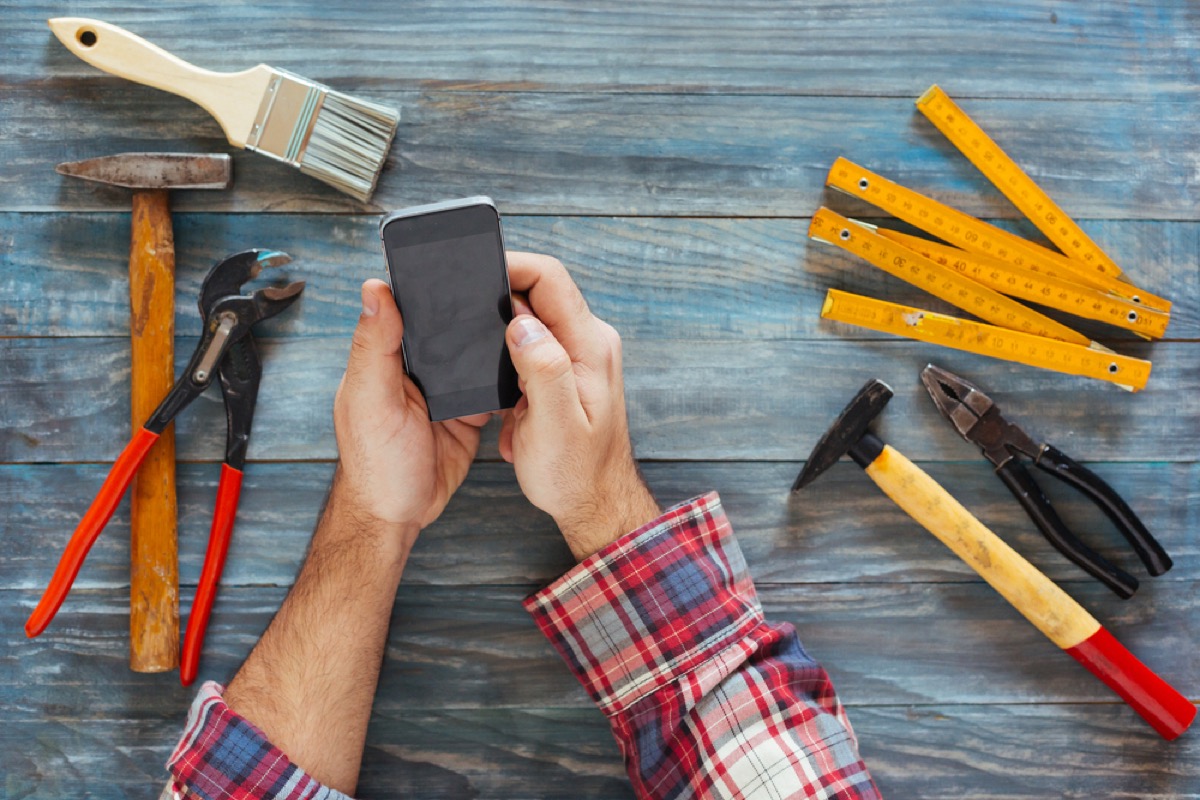 closeup from above of man's hands on phone while leaning on table with tools