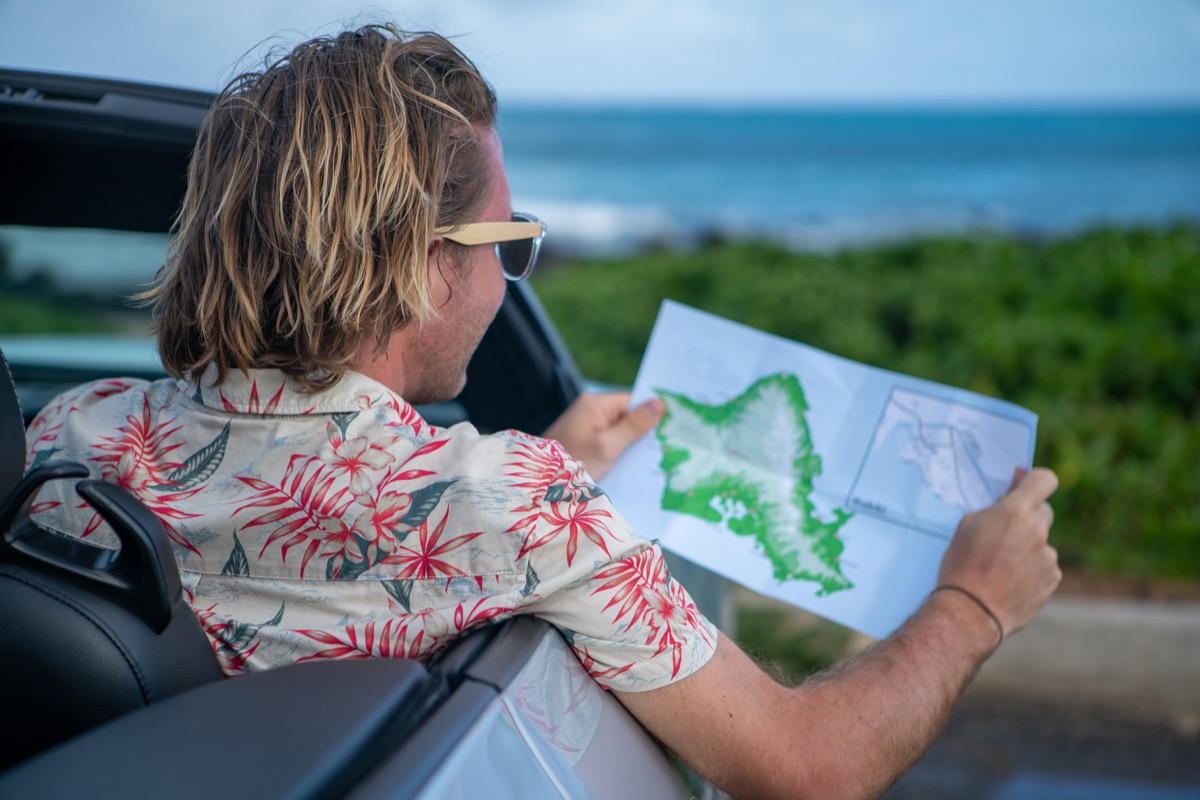 Young man inside convertible car looking at road map for directions, Hawaii