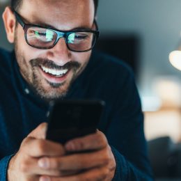 Young man wearing glasses and laughing while looking at jokes on his phone