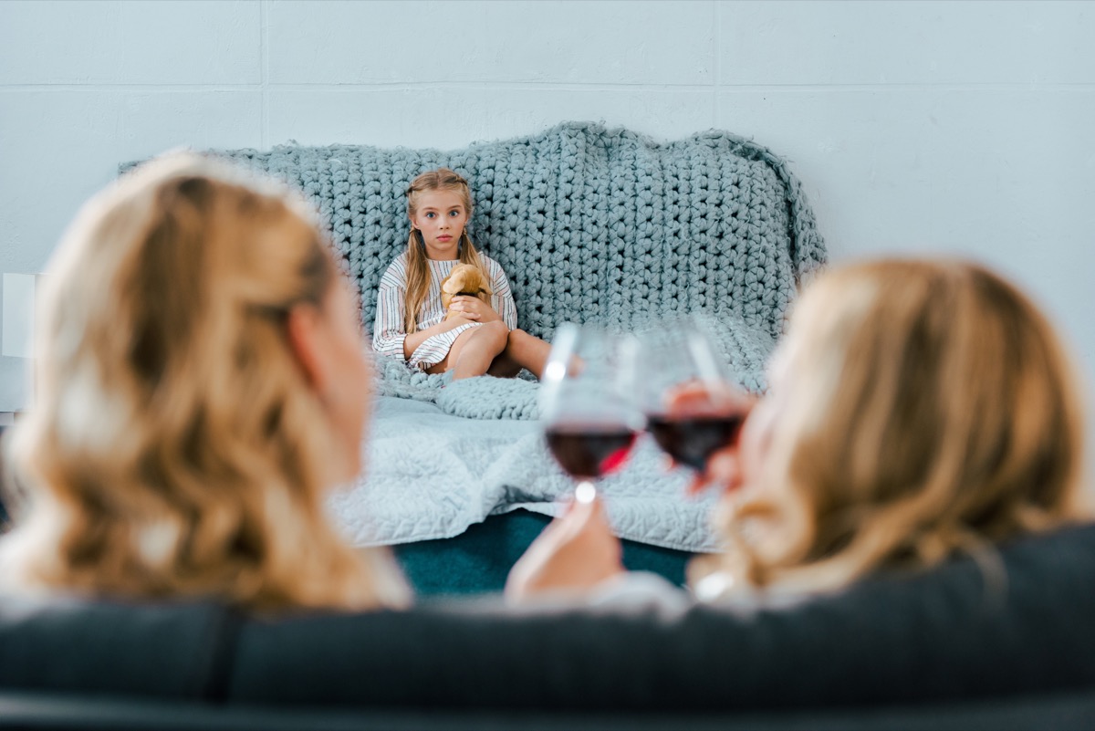 two women drinking wine on the couch while little blonde girl watches