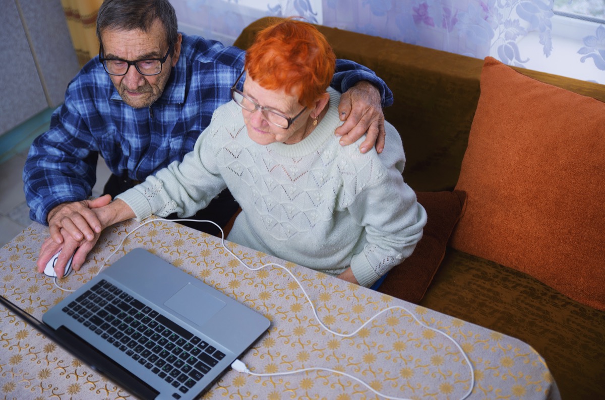 Older man helping older woman use computer