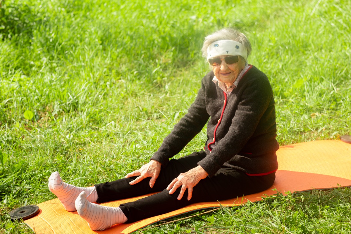Older woman stretching outside in grass on a yoga matt