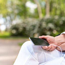 A senior woman with headphones is listening to music on her smart phone in the park