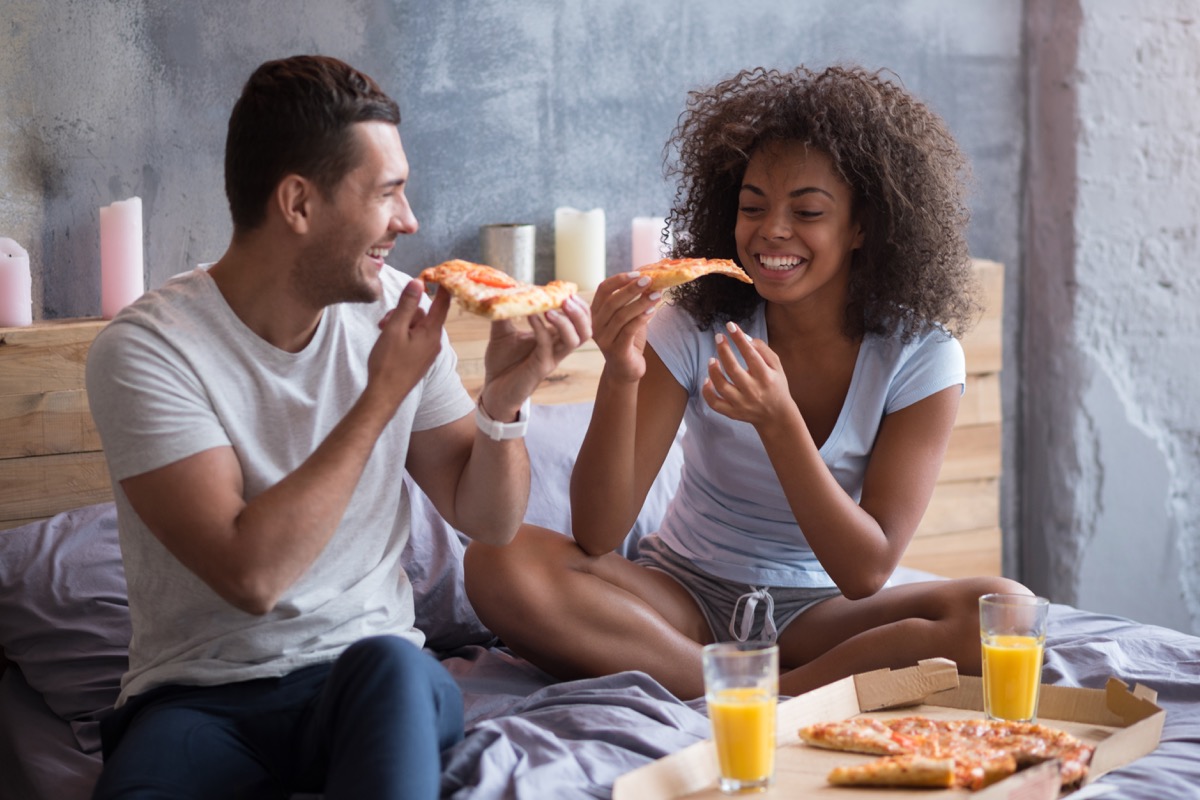 Couple eating pizza in bed