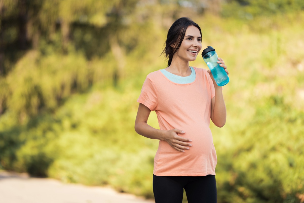 Pregnant woman walking drinking from water bottle