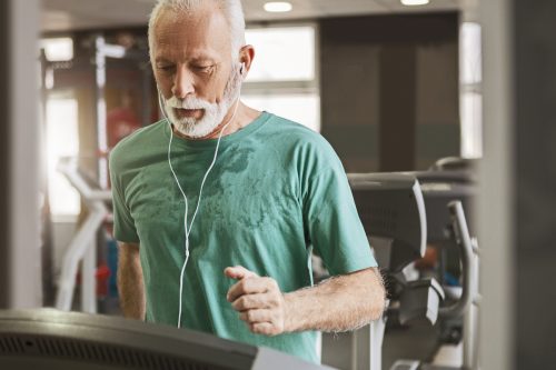 mature man in a green t-shirt walking on the treadmill