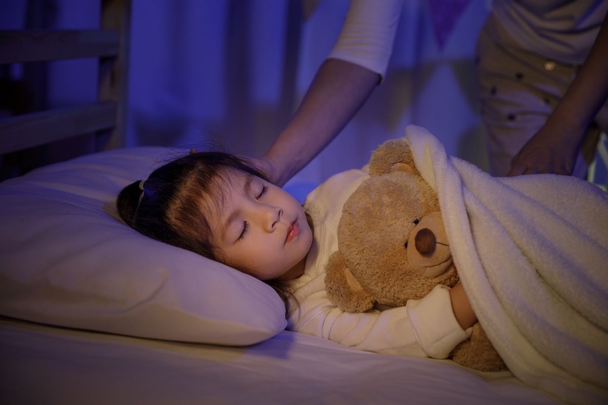 mother putting young asian girl to bed