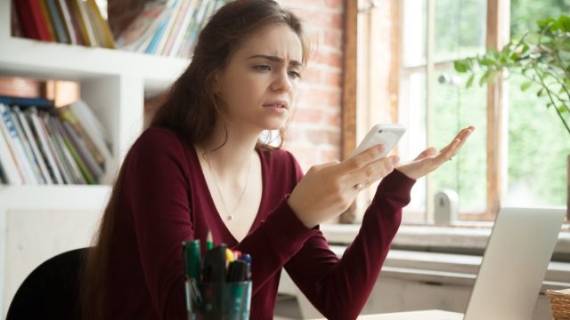 young white woman sitting at desk looking appalled by phone message about to shake her head