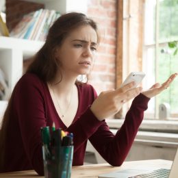 young white woman sitting at desk looking appalled by phone message about to shake her head