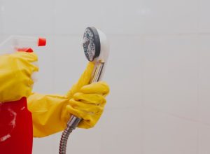 Spraying shower head with cleaning solution and gloves on