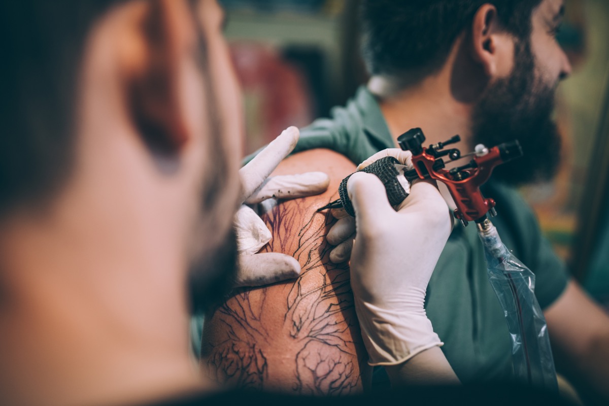 Two men, tattoo artist tattooing a man