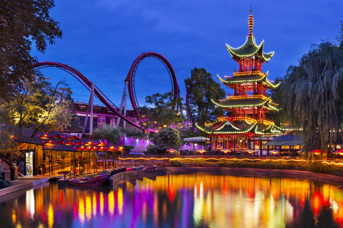 Evening view of Tivoli Gardens with a pagoda on the shore of pond and Daemonen roller coaster, Copenhagen, Denmark