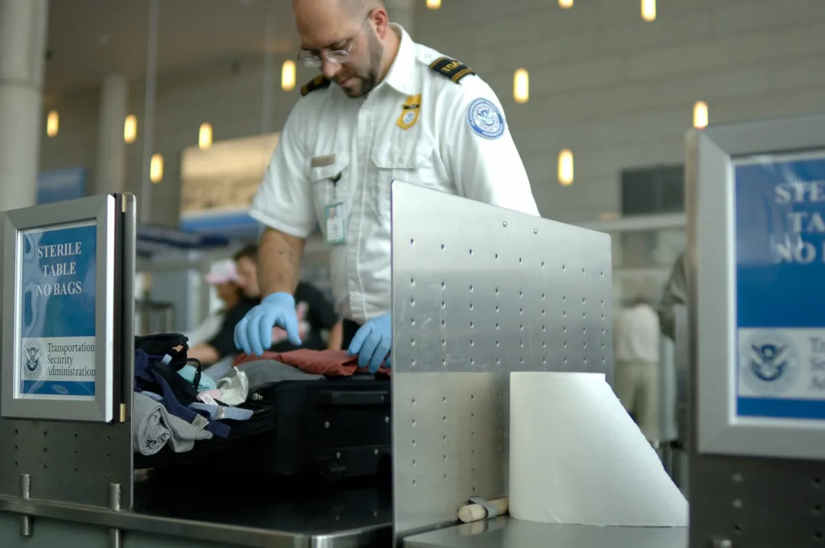 A TSA agent searches baggage at an airport.