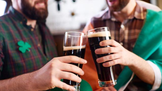 cheerful men in costume clinking beer glasses while celebrating St Patrick day