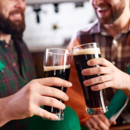 cheerful men in costume clinking beer glasses while celebrating St Patrick day