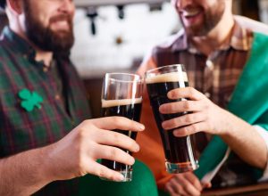 cheerful men in costume clinking beer glasses while celebrating St Patrick day