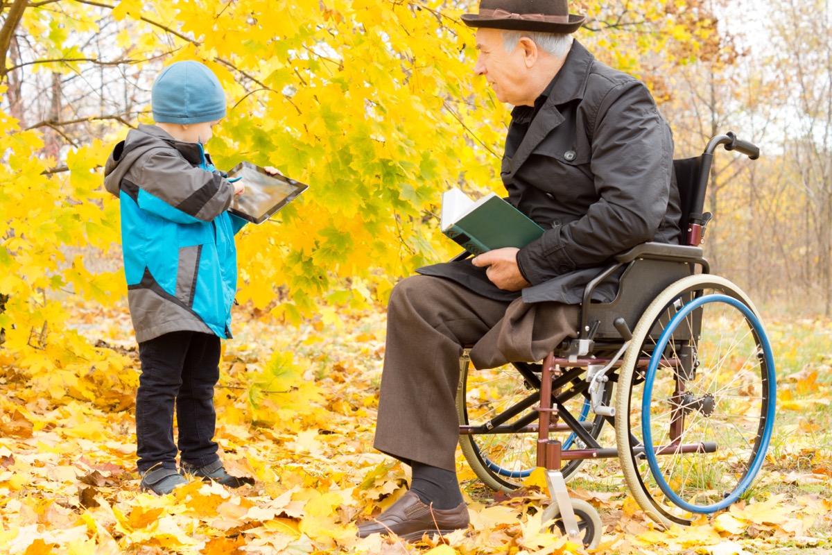 Grandpa in wheelchair with grandson outside in fall reading