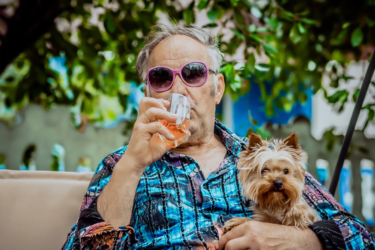 Older man drinking whiskey in sunglasses holding his dog