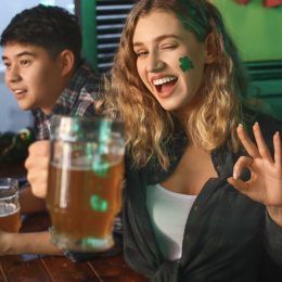 woman with green shamrock sticker on her face and beer in hand celebrating st patrick's day in a bar