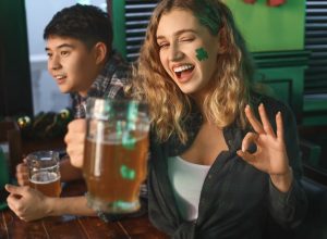 woman with green shamrock sticker on her face and beer in hand celebrating st patrick's day in a bar