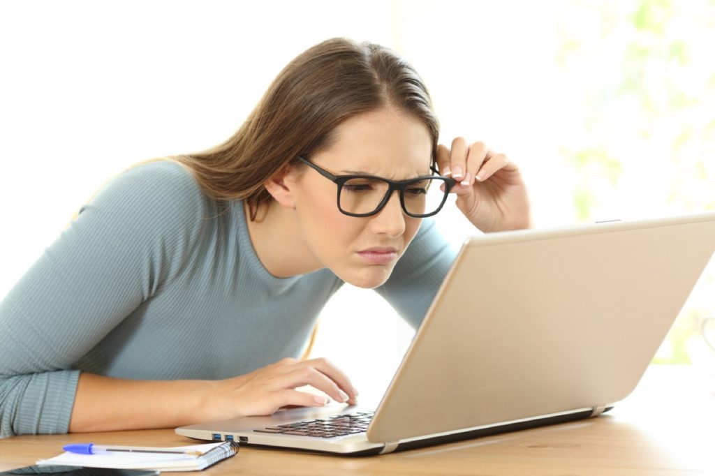 woman wearing glasses reading laptop closely