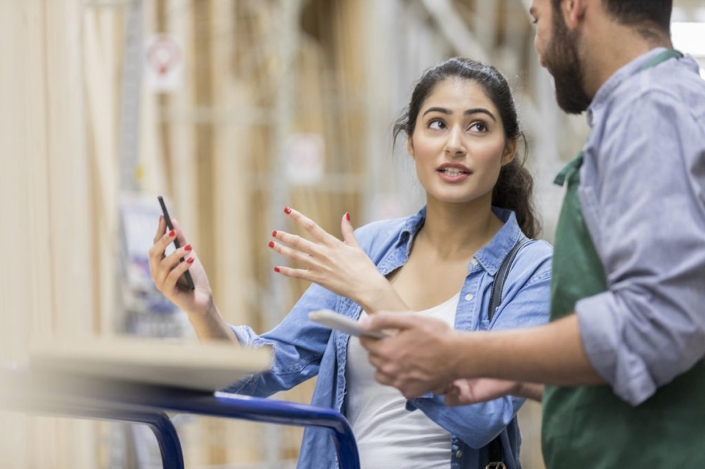 Young woman uses her smart phone to explain her diy project to a hardware store employee