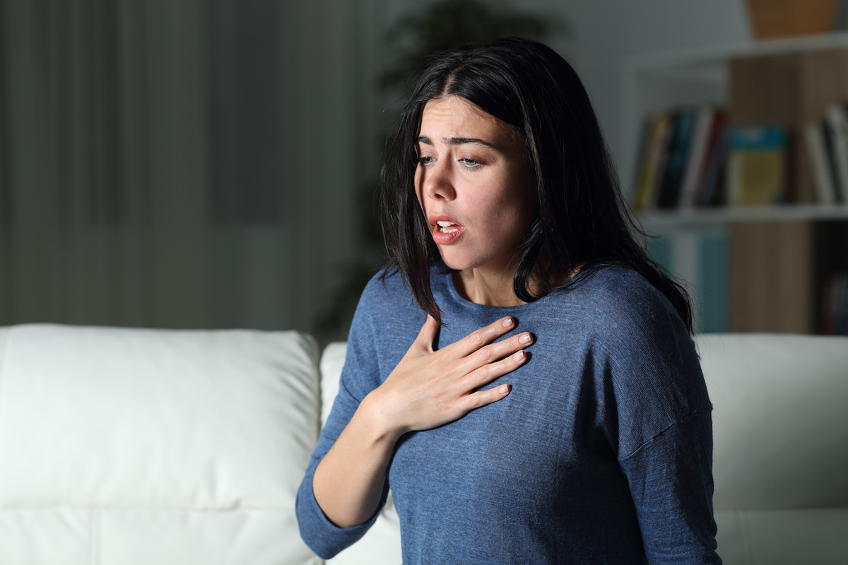 woman alone in house at night has hand on chest as she struggles to breath