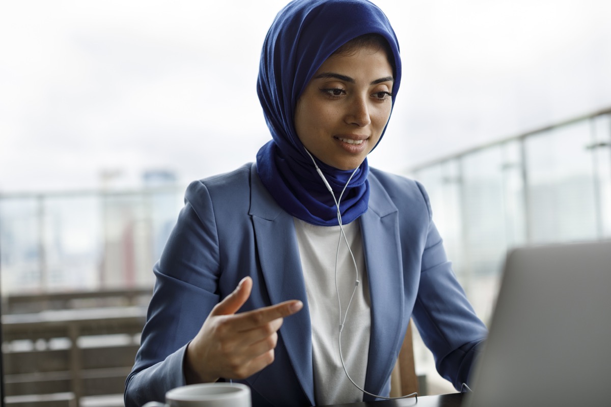 Young woman wearing hijab with headphones working on laptop