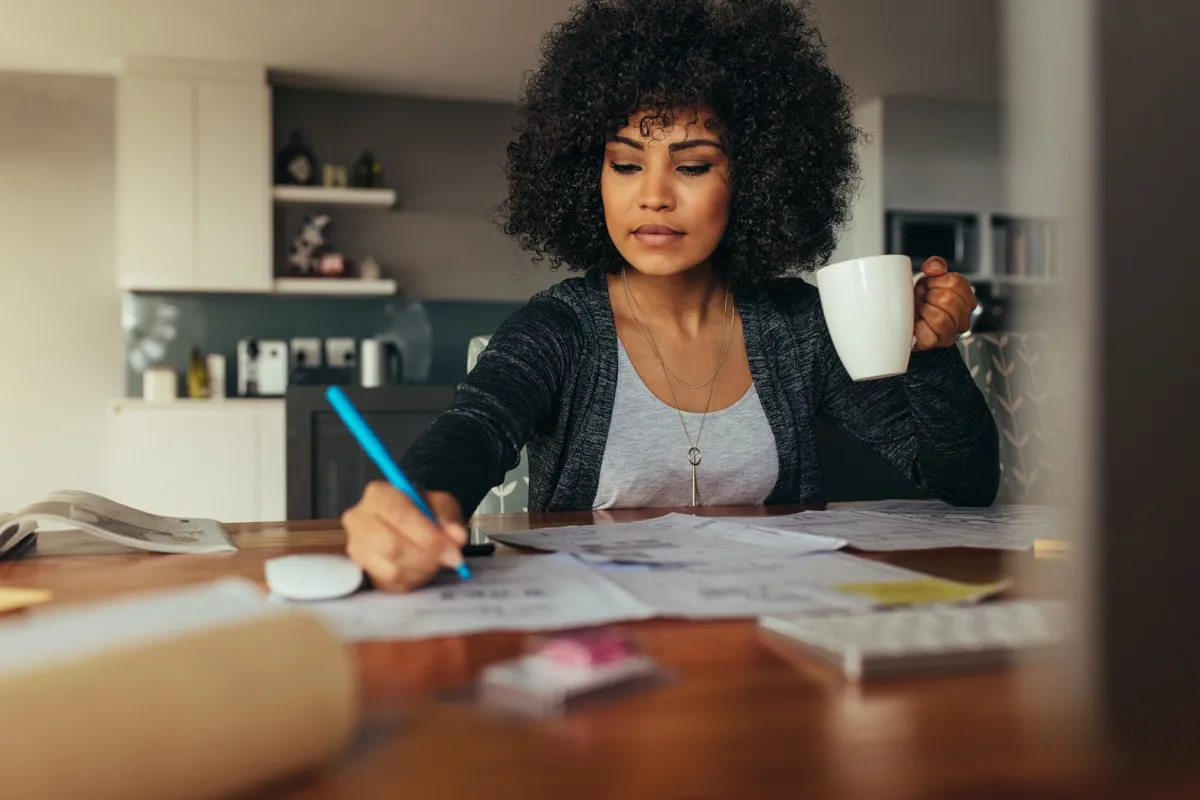 black woman drinking coffee and taking notes while wfh on the computer