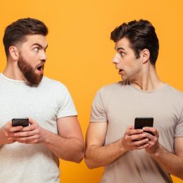 Two men holding phones and looking surprised