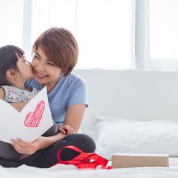 young asian girl giving mother card and kissing her on cheek