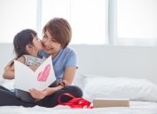 young asian girl giving mother card and kissing her on cheek