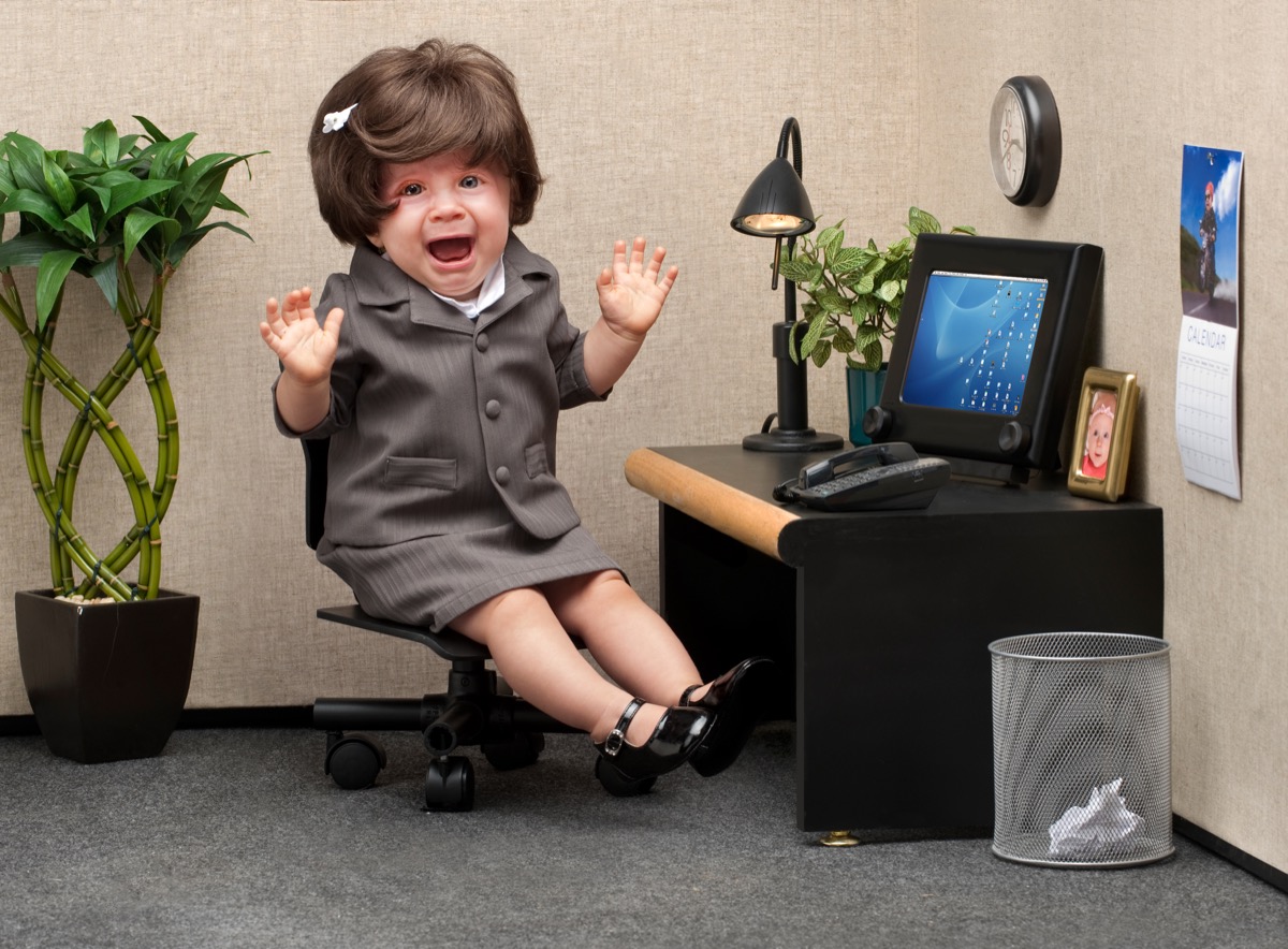 Baby sitting in a business cubicle wearing a business dress with an expression of panic on her face
