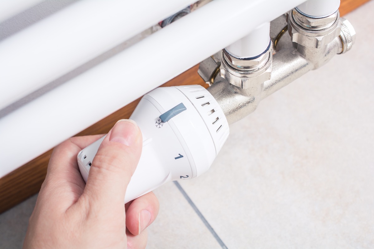 white hand turning thermostat on bathroom radiator