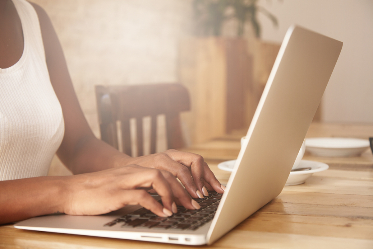 closeup of hands of young black woman at table using laptop