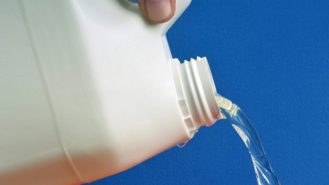 bleach being poured out of white bottle against blue background
