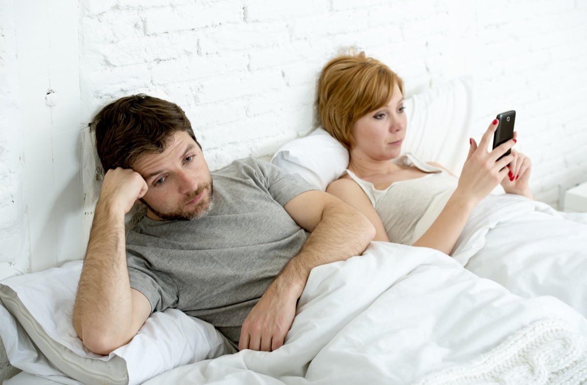 Couple in bed not talking woman texting man bored