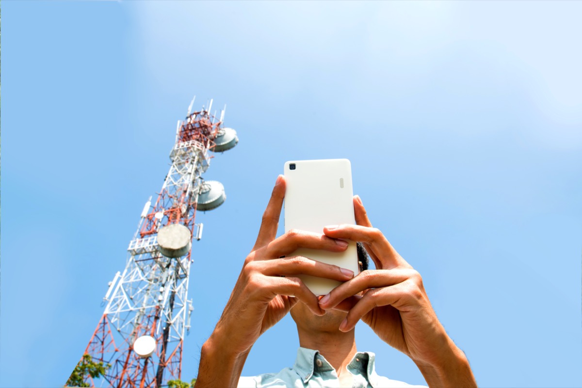 man uses a phone next to a cell phone tower