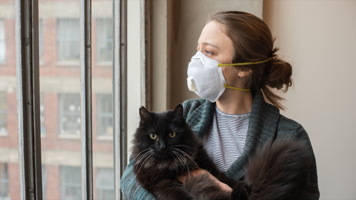 Young woman looks out her downtown apartment window holding her cat. Los Angeles is under shelter-in-place orders due to the Coronavirus pandemic of 2020.