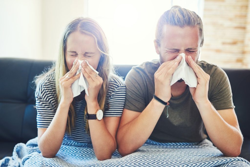 Shot of a young man and woman blowing their noses with tissue at home