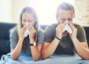 Shot of a young man and woman blowing their noses with tissue at home