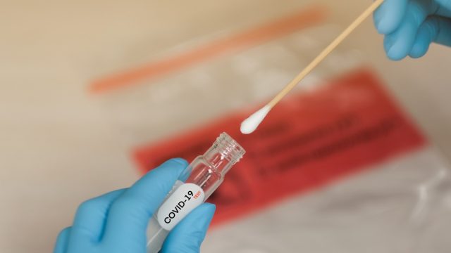 gloved hands in lab putting a swab into coronavirus test vial
