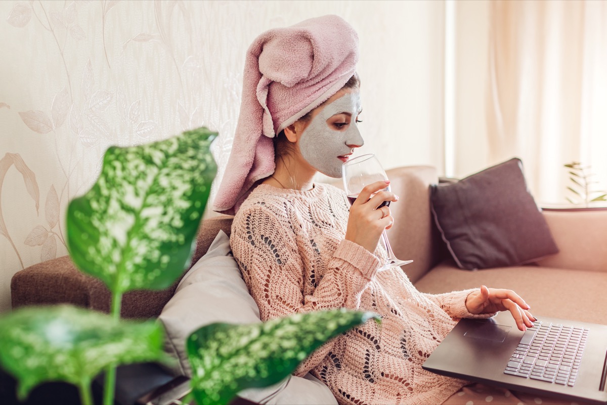 Woman with a facial at home on laptop drinking wine