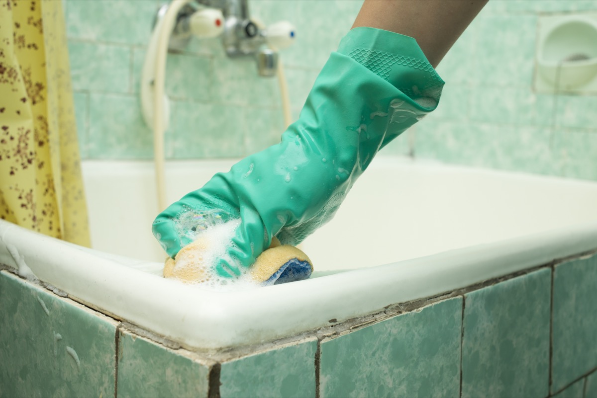 hand with green glove cleaning dirty bath tub