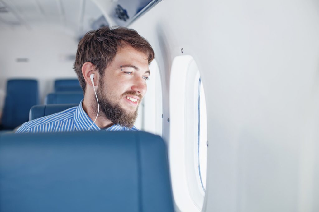 man looking out window of airplane while wearing headphones