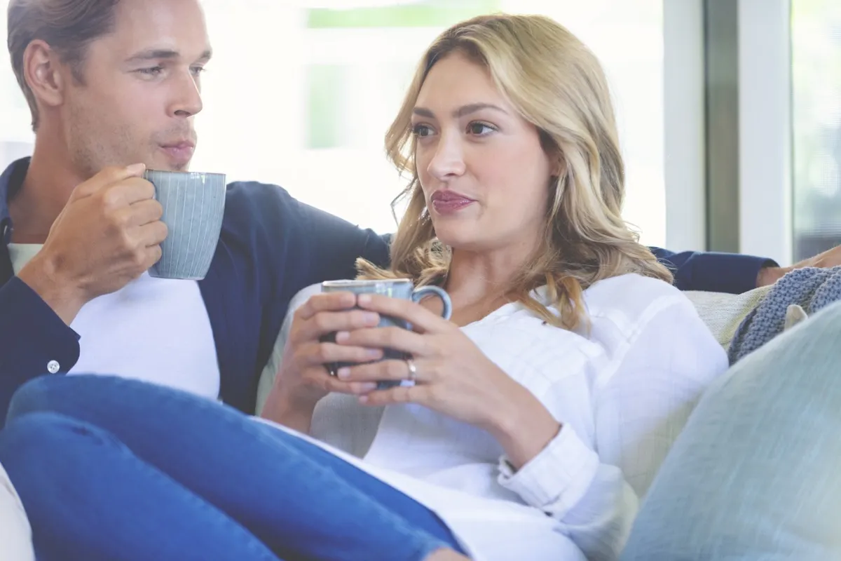 white woman looking uncomfortable while sharing coffee with white man on couch
