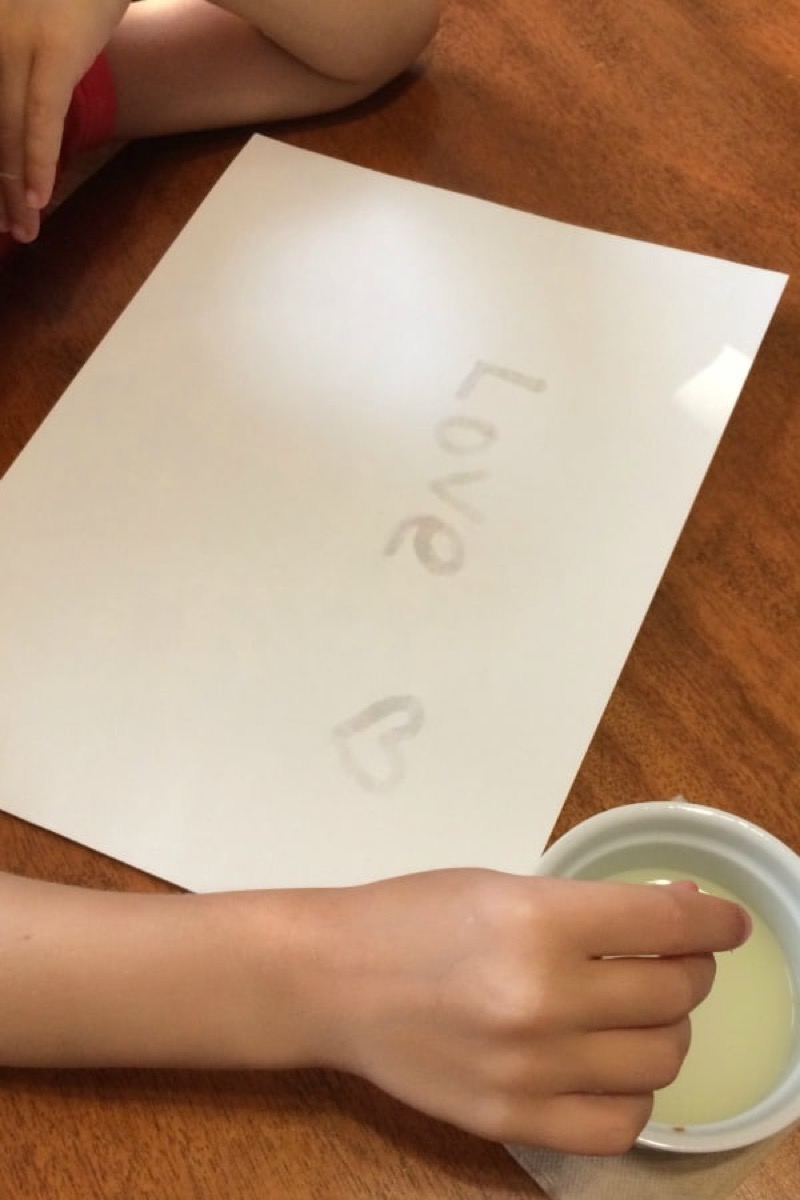 little white child's hand writing love on paper in invisible ink