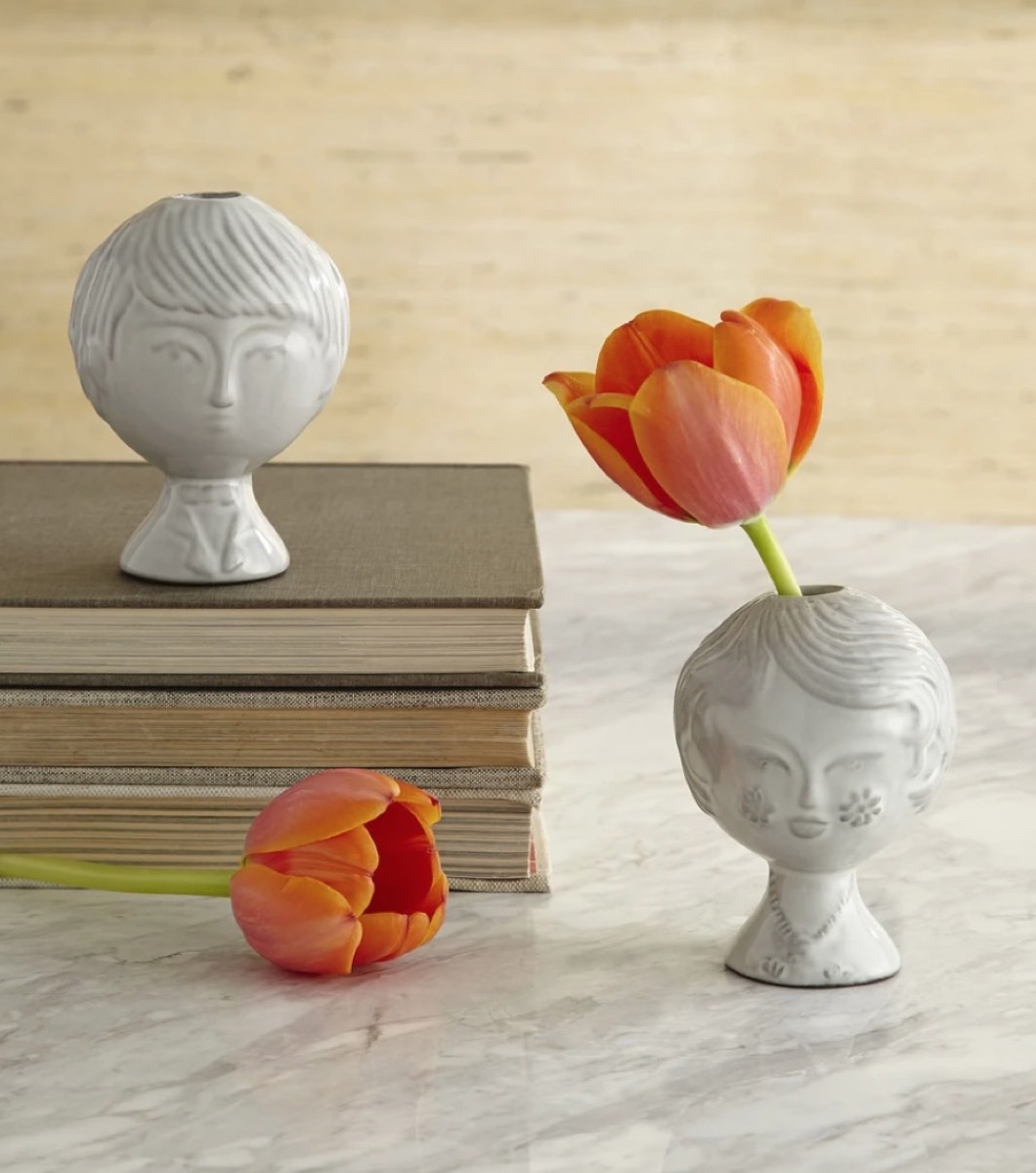 two white ceramic vases with human faces on them holding orange flowers