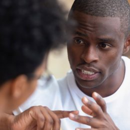 black man having a serious conversation with a woman, whose head is to the camera
